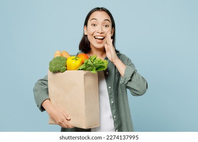 Young woman in casual clothes hold brown paper bag with food products scream share hot news hands near mouth isolated on plain blue background studio portrait. Delivery service from shop or restaurant - Powered by Shutterstock