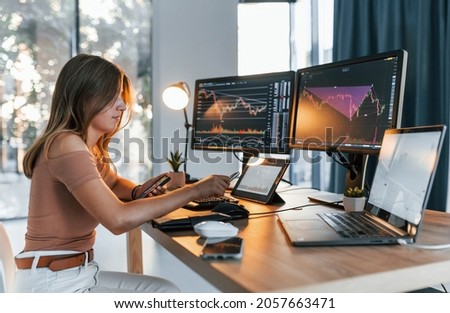 Young woman in casual clothes is in office with multiple screens.
