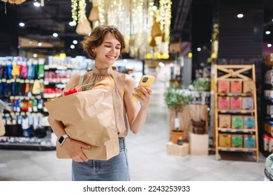 Young woman in casual clothes shopping at supermaket store with craft paper package with groceries using mobile cell phone browsing internet look for recipe inside hypermarket. Gastronomy food concept - Powered by Shutterstock