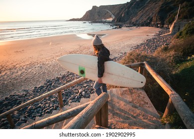 Young woman in casual clothes walk down stairs to beautiful epic beach at sunset or sunrise. Female surfer ready to start surfing lesson at dawn. Millennial lifestyle and hobby. Cinematic wanderlust - Powered by Shutterstock