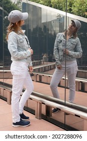 Young Woman In Casual Jeans Looking At The Reflection In The Mirror Outdoors