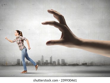 Young woman in casual running away from big hand