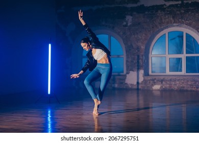 Young woman in casual style - jeans and leather jacket doing ballet in modern studio. Attractive ballerina practices in choreography alone