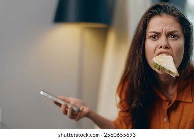 Young woman in casual wear expressing frustration while eating a sandwich and holding a smartphone, showcasing modern lifestyle and multitasking emotions - Powered by Shutterstock