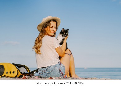 Young Woman With A Cat In A Backpack On The Seashore. Travel Concept With A Pet.