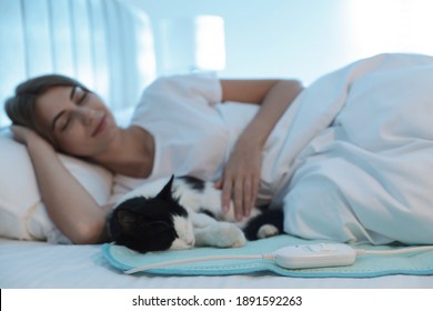 Young Woman And Cat In Bed With Electric Heating Pad, Focus On Cable