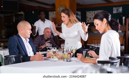 Young Woman Catching Her Husband With Mistress In Restaurant. Cheating In Marriage Concept