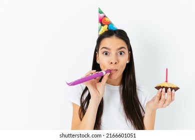 Young Woman Celebrating Surprised Blows In Kazoo Holding Birthday Cake, White Studio Background