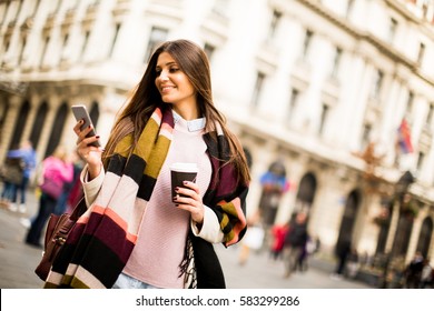 Young Woman With Cell Phone And Coffee To Go Walking On The Street