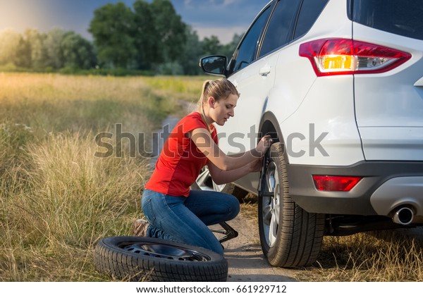 Young woman\
changing flat tire on the rural\
road