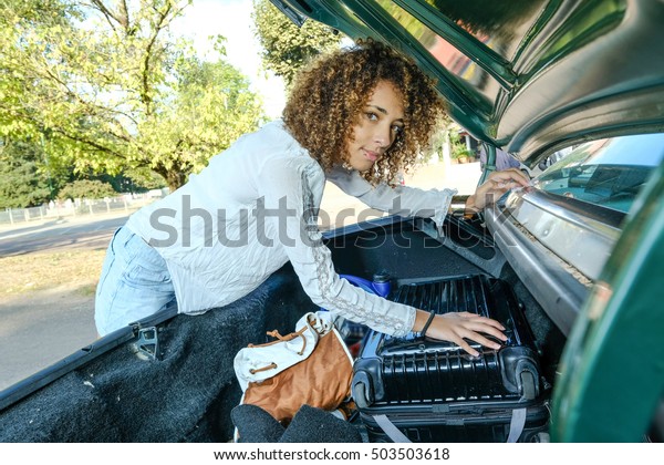 Young woman changing the wheel of her american\
car on a parking