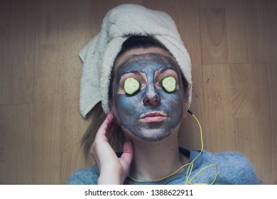 Young woman with charcoal facemask and with cucumber on her eyes relaxing at a spa - Powered by Shutterstock