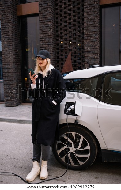 Young woman is charging an electric car. The\
rental car is charging at the charging station for electric\
vehicles. Car sharing.