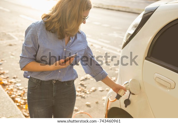 Young woman charging an electric car. The rental\
car is charging at the charging station for electric vehicles. Car\
sharing.