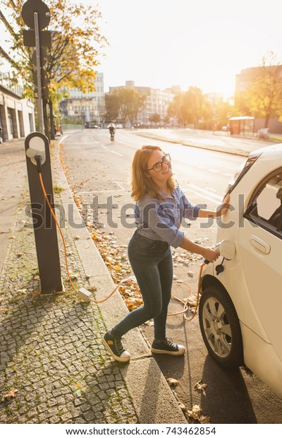 Young woman is charging an electric car. The\
rental car is charging at the charging station for electric\
vehicles. Car sharing.