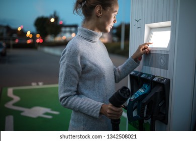 Young woman charging an electric vehicle. Car sharing concept.