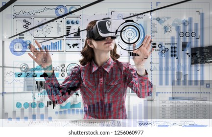 Young woman in checkered shirt using VR headset with digital media interface while sitting inside bright office building. Virtual reality technologies for education
