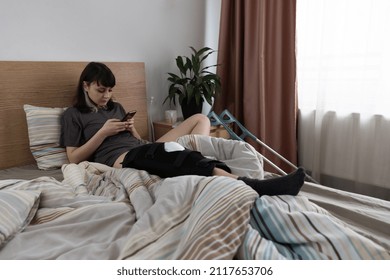 Young Woman Checking Her Phone In Bed, After An ACL Surgery.