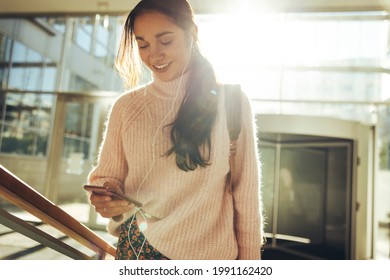Young Woman Checking Social Media Before Going For Class In College. Student Climbing Stairs And Looking At Mobile Phone.