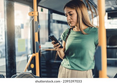 Young woman checking social media on phone in bus. Beautiful girl with long hair using smartphone for reading or writing message while standing in city bus. - Powered by Shutterstock