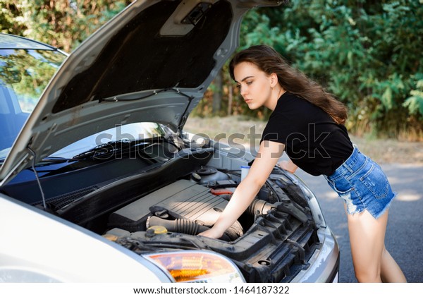 Young woman checks car engine and tries to\
repair car by herself.