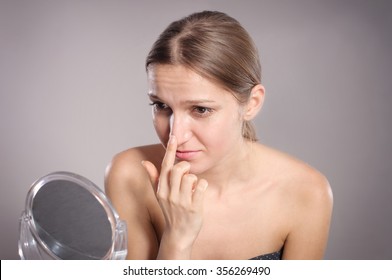 Young woman checks her nose in the mirror