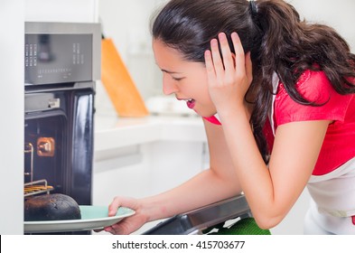 Young Woman Chef Looking Into Oven With Frustrated Facial Expression, Holding Black Burnt Bread On Tray