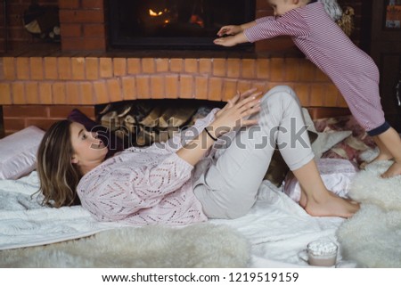 young woman with a child. Mom and son are fooling around, having fun near the fireplace.