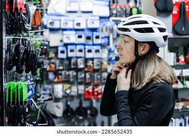 A young woman chooses a bicycle helmet in a bike shop. Portrait of young woman choosing bicycle helmet in sport shop. Focus on helmet - Powered by Shutterstock