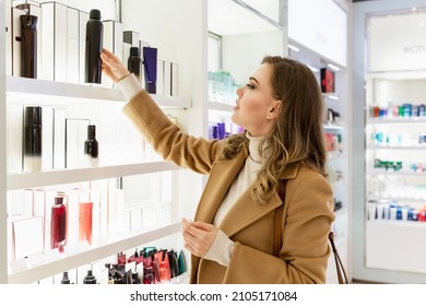 Young woman chooses a body cosmetic product in a store. Beautiful blonde in a beige coat. Personal care and cosmetology.