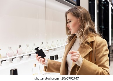 Young woman chooses perfume in the store. Smiling beautiful blonde in a beige coat. Individual scent and expensive cosmetics. 