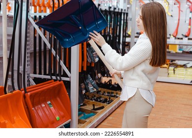 Young woman chooses shovel for snow removal in hardware store.