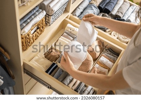 A young woman chooses which bra to wear while standing in front of a neatly arranged wardrobe. The concept of underwear storage and space organization. Top view. 