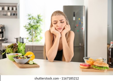 Young woman choosing between diet and unhealthy food in kitchen