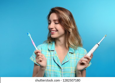 Young woman choosing between manual and electric toothbrushes on color background