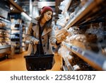 Young woman choosing bread while buying groceries in supermarket. 