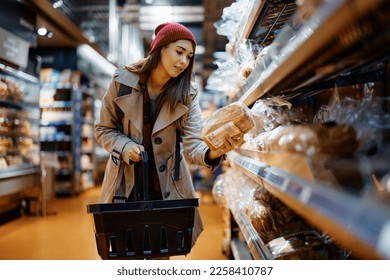 Young woman choosing bread while buying groceries in supermarket.  - Powered by Shutterstock