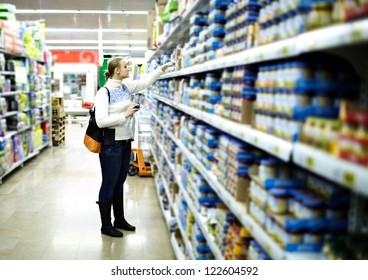 Young Woman Is Choosing Food For Her Child At The Food Store. Wide Shot, Shallow Dof.