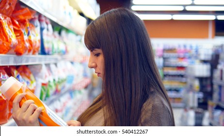 Young Woman Choosing Household Chemicals In Supermarket. Beautiful Girl Selects Fabric Softener Or Washing Powder At The Store And Put It A Shopping Cart. Department Of Cleaning Product And Home Care