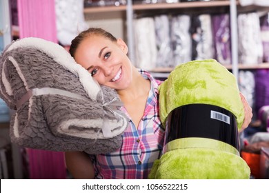 Young Woman Choosing New Coverlet For Home In Textile Shop