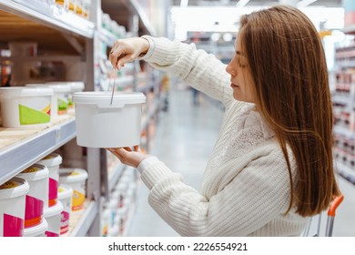 Young Woman is Choosing Paint in Buckets for Walls in in Hardware Diy Store. Acrylic paint for concrete surfaces in plastic buckets