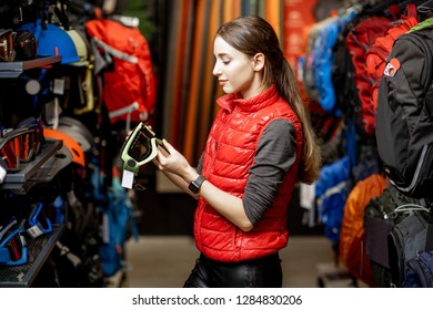 Young woman choosing some sports equipment looking on the ski glasses in the sports shop