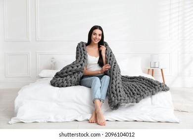 Young Woman With Chunky Knit Blanket On Bed At Home