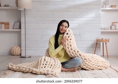 Young Woman With Chunky Knit Blanket On Floor At Home