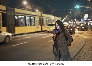 young woman in the city at night while using a smartphone - Powered by Shutterstock