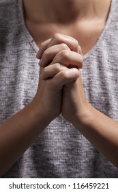 A young woman clasps her hands in prayer.