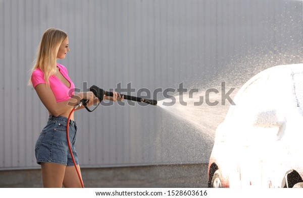 Young woman cleaning automobile with high pressure\
water jet at car wash