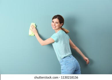 Young Woman Cleaning Color Wall With Rag