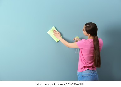 Young Woman Cleaning Color Wall With Rag