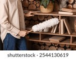 Young woman cleaning dust on book shelves in room, closeup